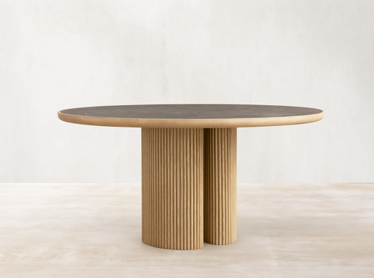 Astor Round Dining Table with a dark marble top and ribbed oak wood base, set on a wooden floor in a neutral room.