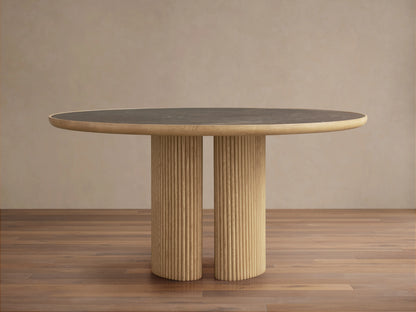 Astor Round Dining Table with a dark marble top and ribbed oak wood base, set on a wooden floor in a neutral room.