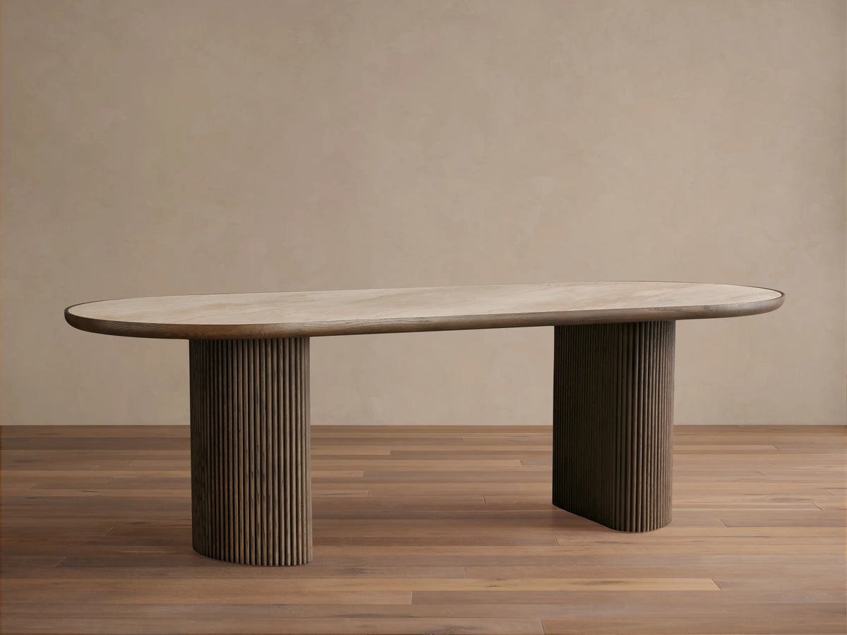 Astor Dining Table: Oval light oak veneer top with dark trim, two dark reeded cylindrical oak bases, front view on wood floor.