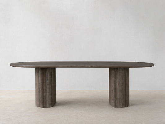 Astor Dining Table with elongated oval top in oak veneer, supported by two ribbed, cylindrical oak wood legs, on a wooden floor.