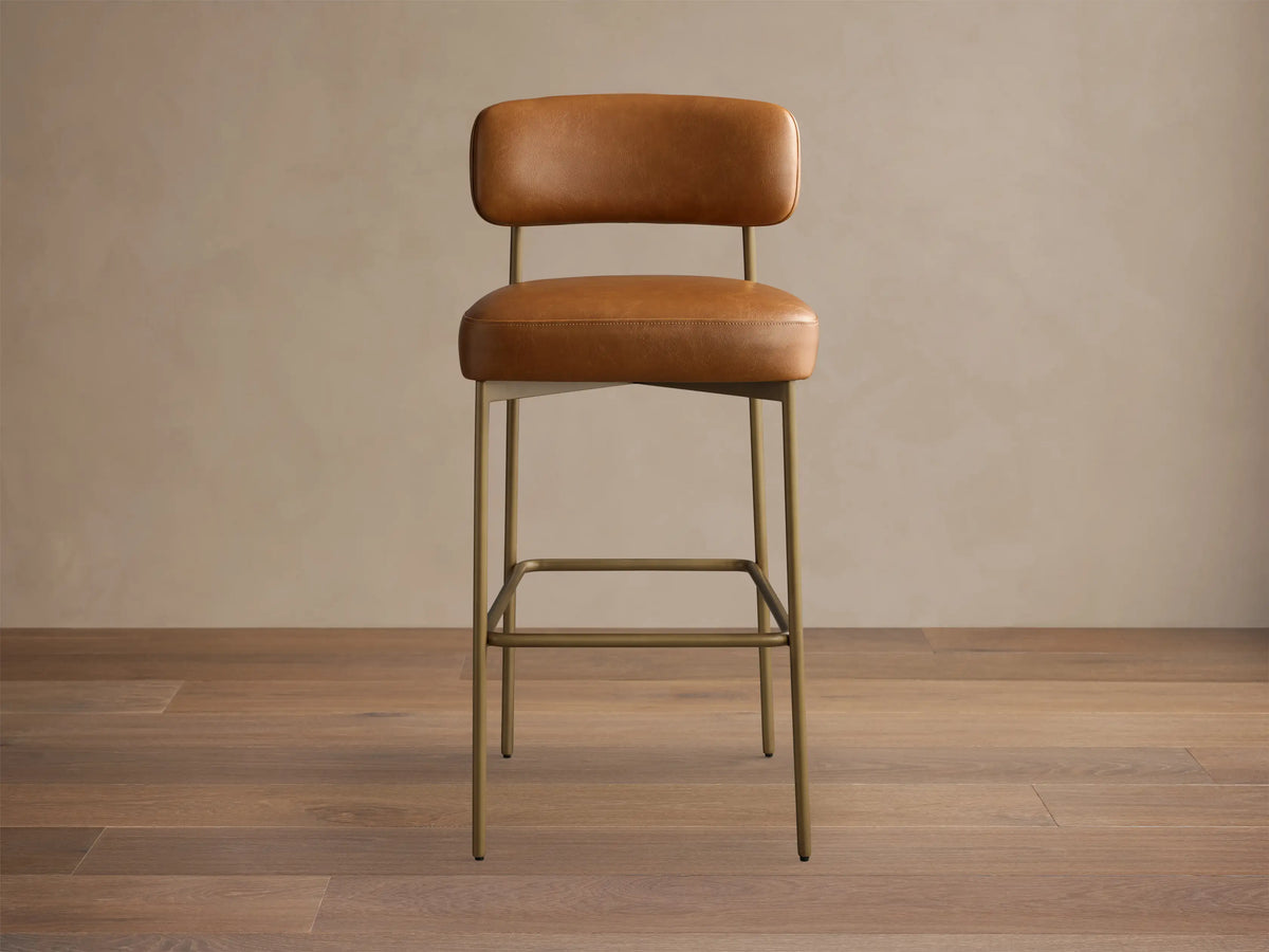 Front view of a brown leather bar stool with a padded seat and back, on a slim gold metal frame with a square footrest.