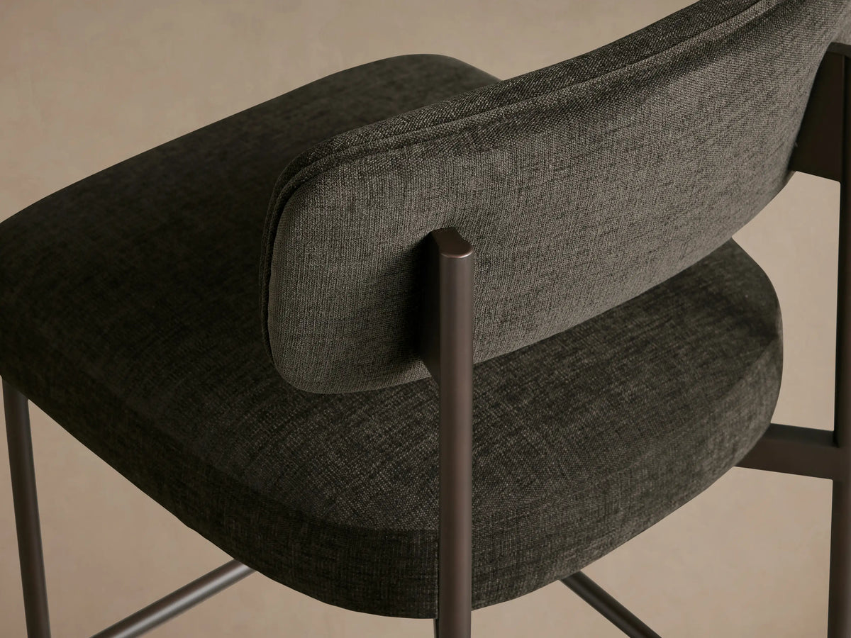 Billie Stool: Dark gray upholstered stool with antiqued iron frame, padded seat & back, on a wooden floor.