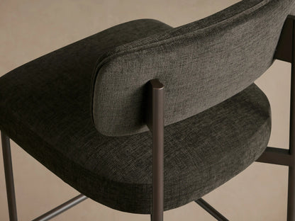 Billie Stool: Dark gray upholstered stool with antiqued iron frame, padded seat & back, on a wooden floor.