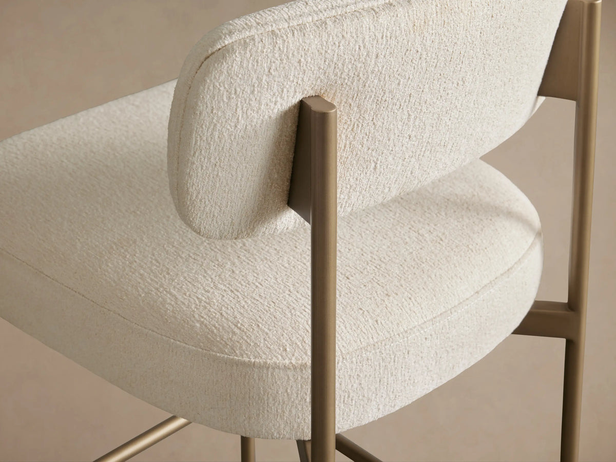 Billie Stool, off-white upholstered seat & backrest, antiqued gold metal frame, front view on a wooden floor.