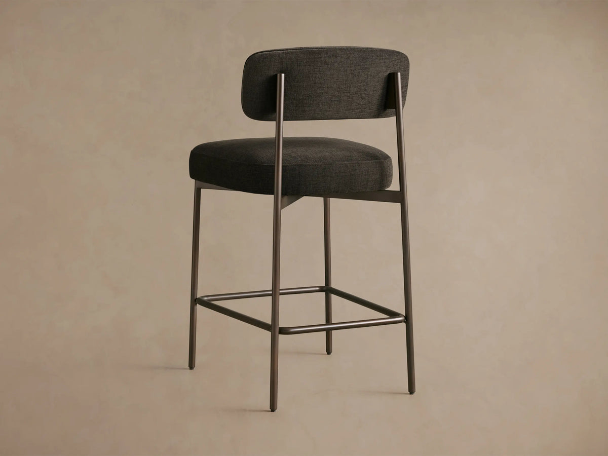 Billie Stool: Close-up, angled view of dark grey woven fabric seat and curved backrest, with antiqued iron frame.