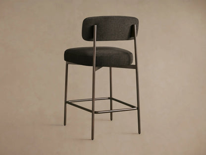 Billie Stool: Close-up, angled view of dark grey woven fabric seat and curved backrest, with antiqued iron frame.