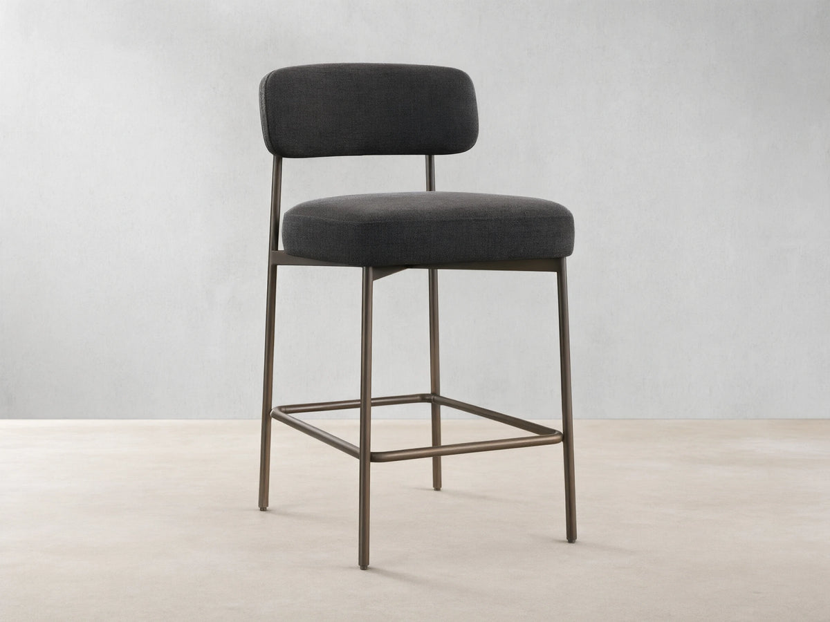 Billie Stool, dark gray fabric seat & back on antiqued iron frame, front-right view on a wooden floor.