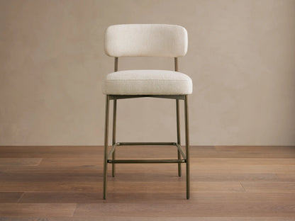 Billie Stool: Cream textured fabric seat & back on an antiqued bronze metal frame, with a footrest, on a wooden floor.