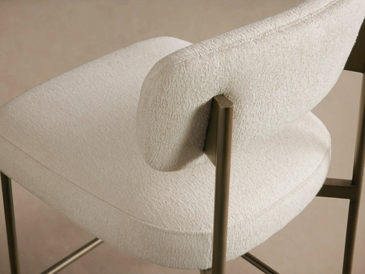 Front view Billie Stool with off-white textured upholstered seat & back, antiqued dark metal frame, on wood floor.