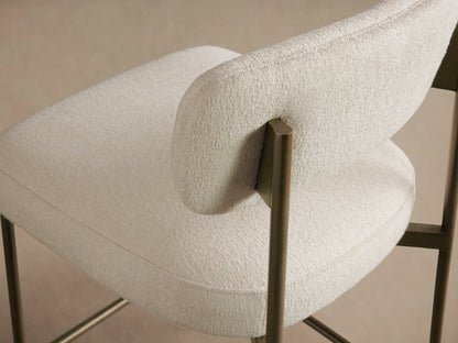 Front view Billie Stool with off-white textured upholstered seat & back, antiqued dark metal frame, on wood floor.