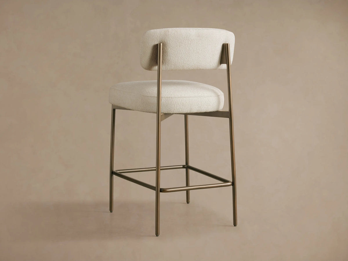 Close-up of Billie Stool's textured off-white fabric seat and curved backrest, supported by an antiqued bronze iron frame.