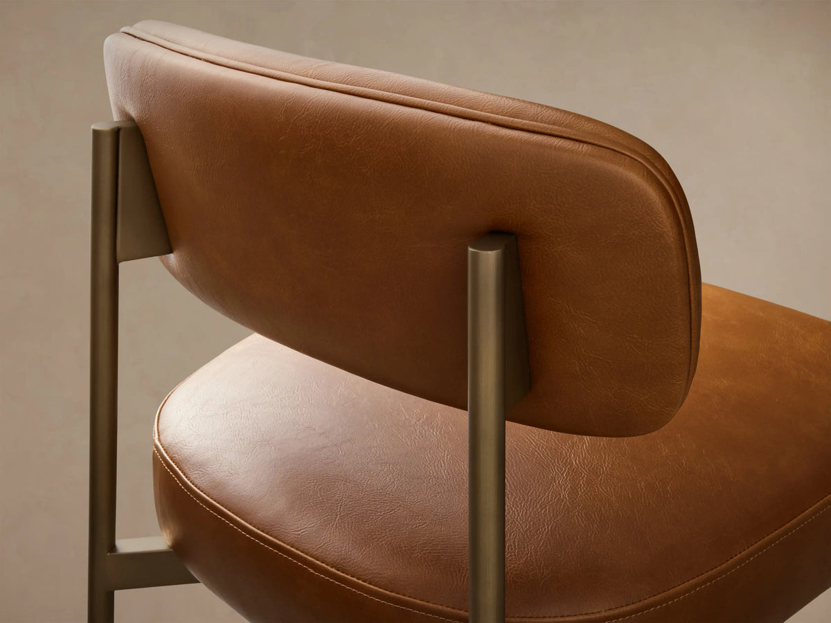 Front view of a Camel Billie Stool in Faux Leather with an antiqued gold iron frame, padded seat, back, and footrest bar.