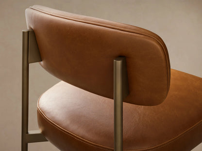 Front view of a Camel Billie Stool in Faux Leather with an antiqued gold iron frame, padded seat, back, and footrest bar.