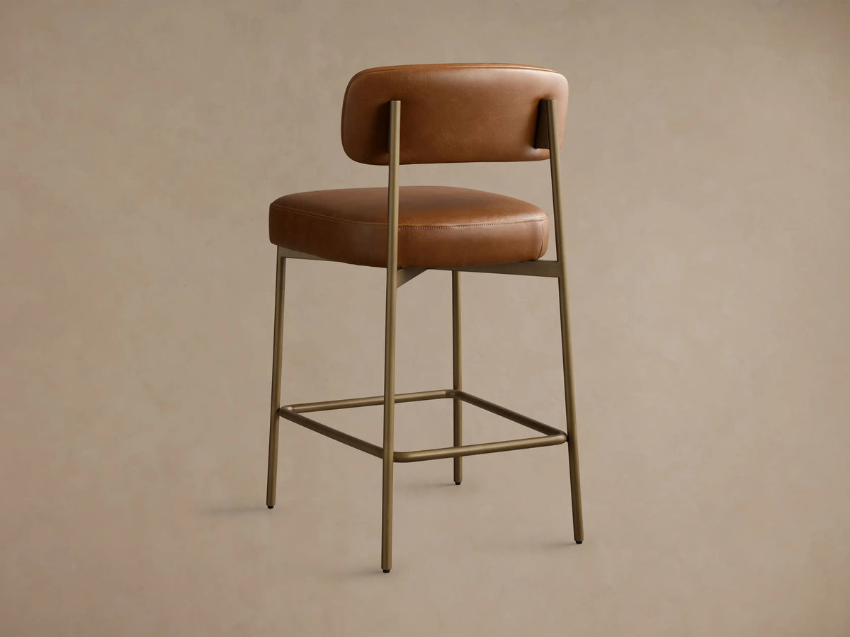 Close-up, angled view of the brown faux leather Billie Stool, highlighting the padded backrest, seat, and antiqued iron frame.