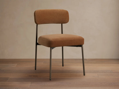 Billie Dining Chair with warm brown upholstered seat and back, antique bronze frame, angled right on a light wooden floor.