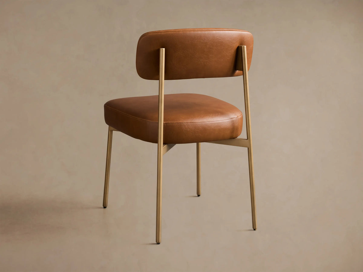 Close-up of the brown faux leather Billie Dining Chair, highlighting the padded seat, backrest, and brass-toned frame.