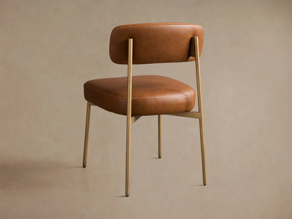 Close-up of the brown faux leather Billie Dining Chair, highlighting the padded seat, backrest, and brass-toned frame.