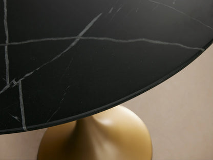 Saint Germain Bistro Table with a round black marble top and a sleek, gold-finished steel base, set on wooden flooring.