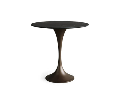 Saint Germain Bistro Table with a black marquina marble top and sleek bronze steel base on a hardwood floor, against a beige wall.