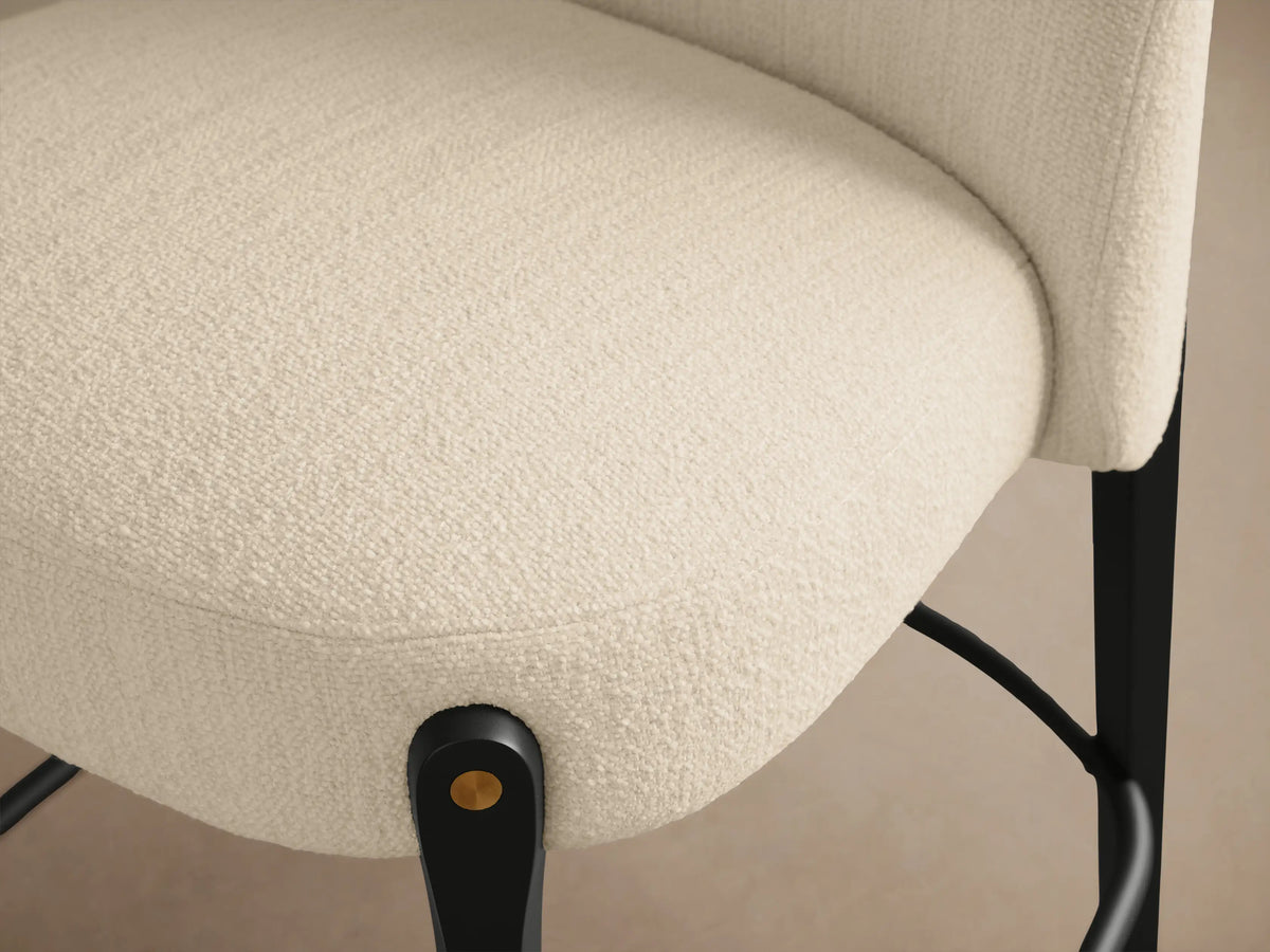 Front view of a Bottoni Stool with cream upholstered seat/back, dark wooden legs, and brass accents, on a wood floor.