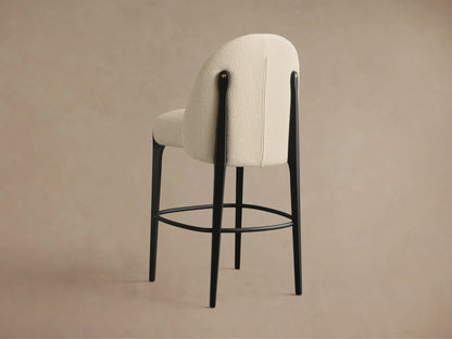 Close-up of Bottoni Stool's cream textured upholstery, black frame, and brass tack accent from a slightly elevated angle.