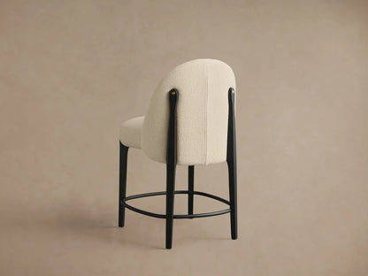 Close-up of Bottoni Stool's cream bouclÃ© upholstered seat and back, with black leg and brass accent on light beige background.