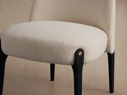 Front view of Bottoni Dining Chair with cream bouclé upholstery, dark wooden legs, and brass accents, on a wood floor.
