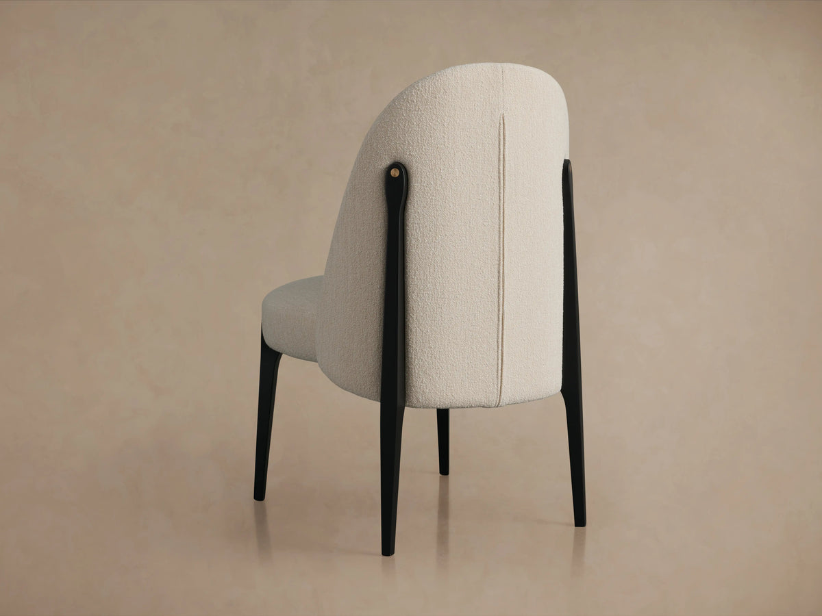 Bottoni Dining Chair, angled close-up: off-white textured upholstery, black legs with round brass accent.
