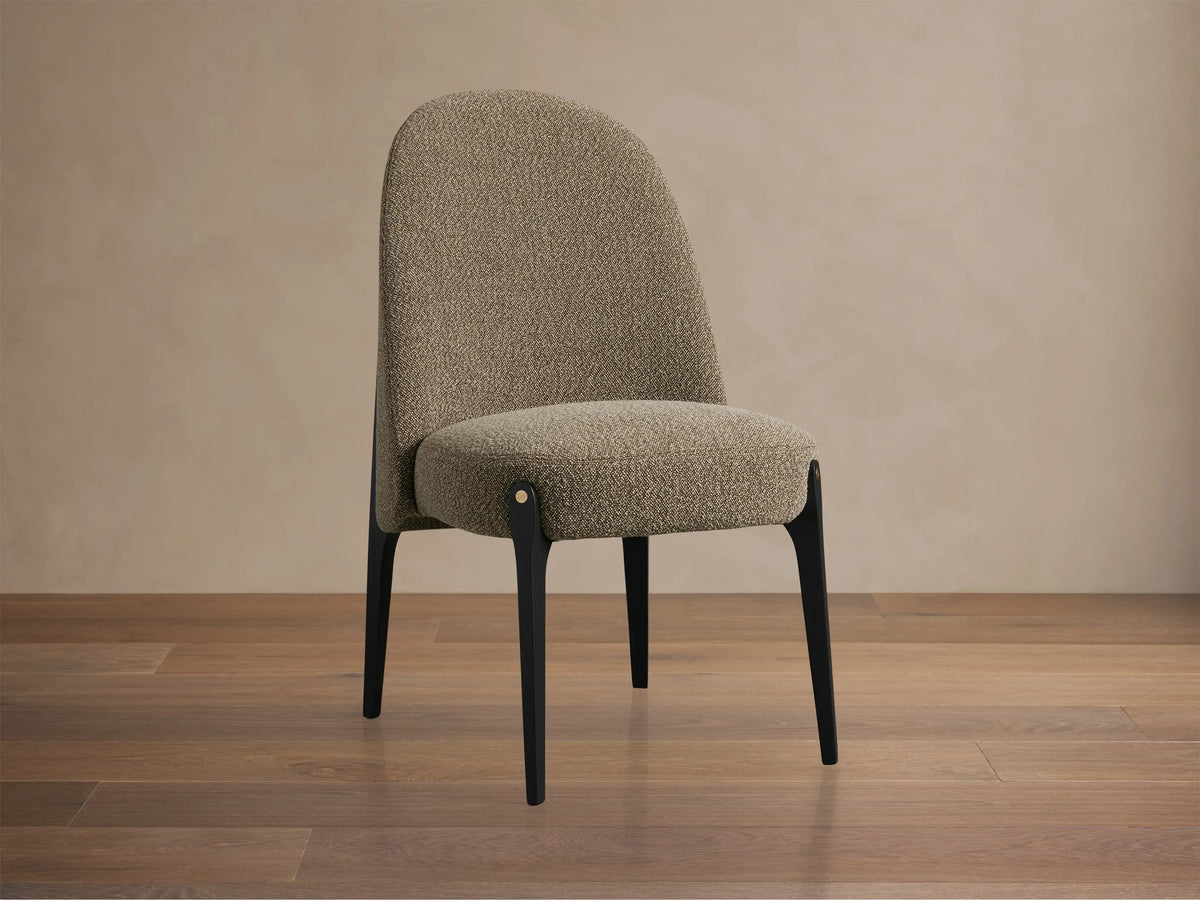 Bottoni Dining Chair, upholstered in light brown textured fabric, with dark legs and brass accents, angled on a wood floor.