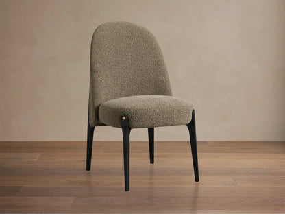 Bottoni Dining Chair, upholstered in light brown textured fabric, with dark legs and brass accents, angled on a wood floor.