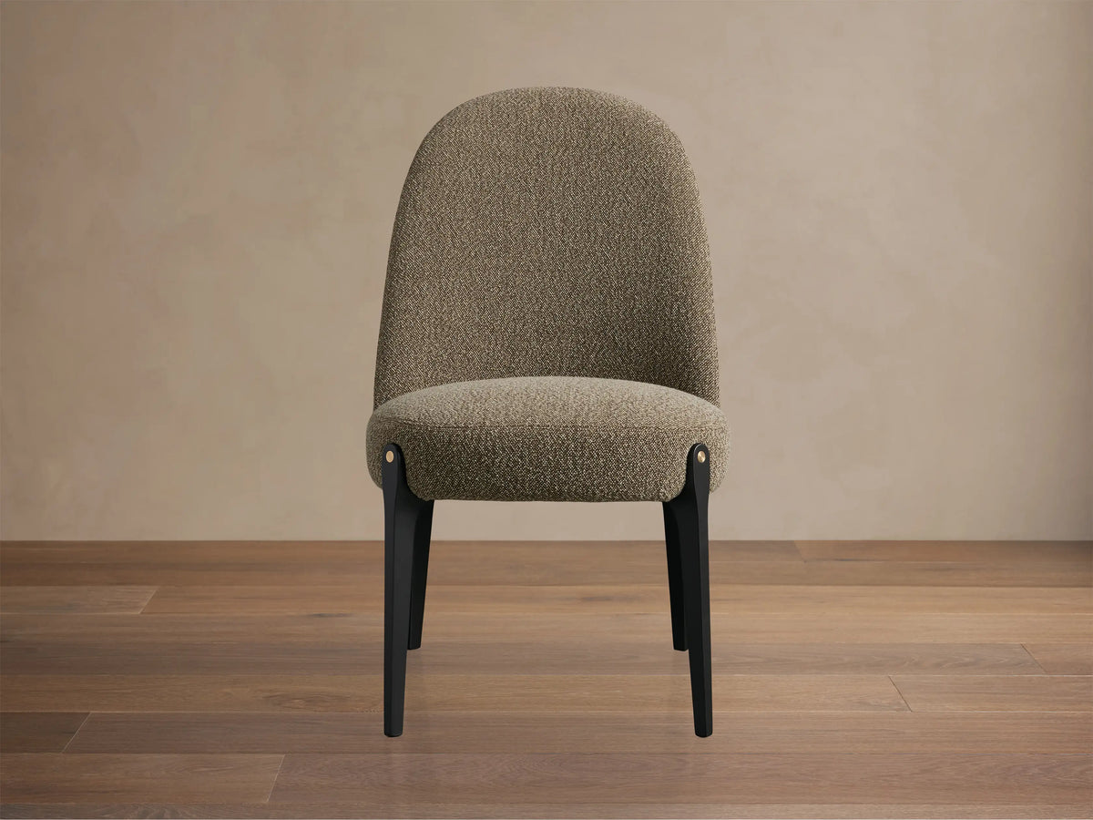 Bottoni Dining Chair, upholstered in light brown textured fabric, with dark legs and brass accents, angled on a wood floor.