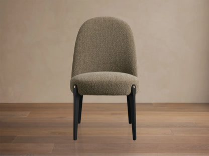 Bottoni Dining Chair, upholstered in light brown textured fabric, with dark legs and brass accents, angled on a wood floor.