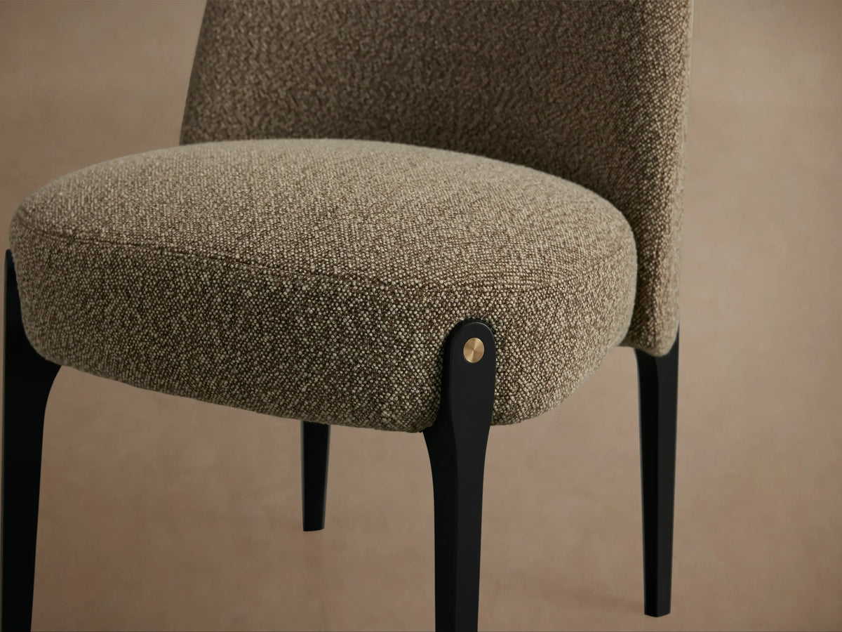 Bottoni Dining Chair, front view. Curved upholstered back and seat in textured brown fabric. Tapered black legs, brass accents.