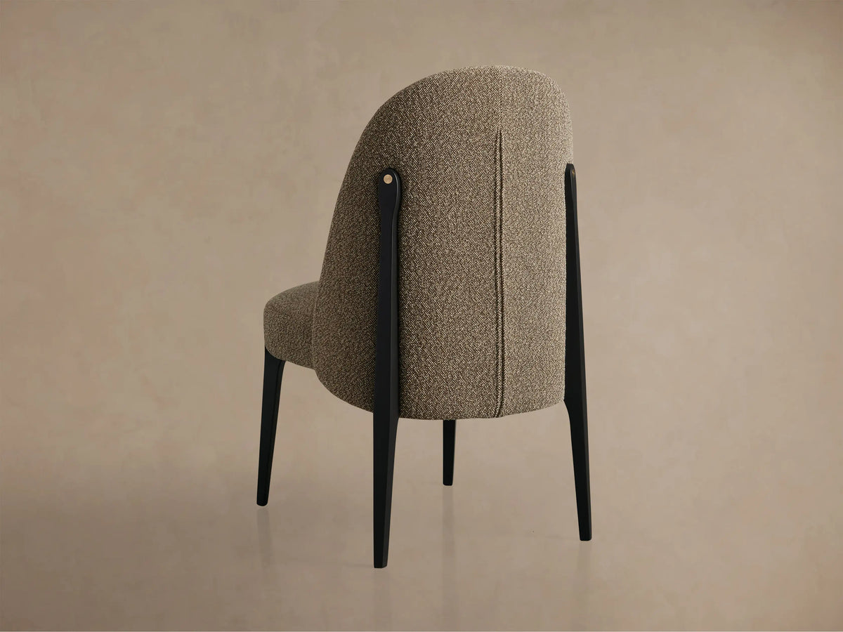 Close-up of a Bottoni Dining Chair, upholstered in textured brown fabric, with dark wooden legs and a brass accent.