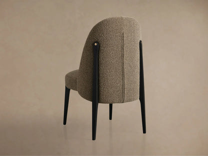 Close-up of a Bottoni Dining Chair, upholstered in textured brown fabric, with dark wooden legs and a brass accent.