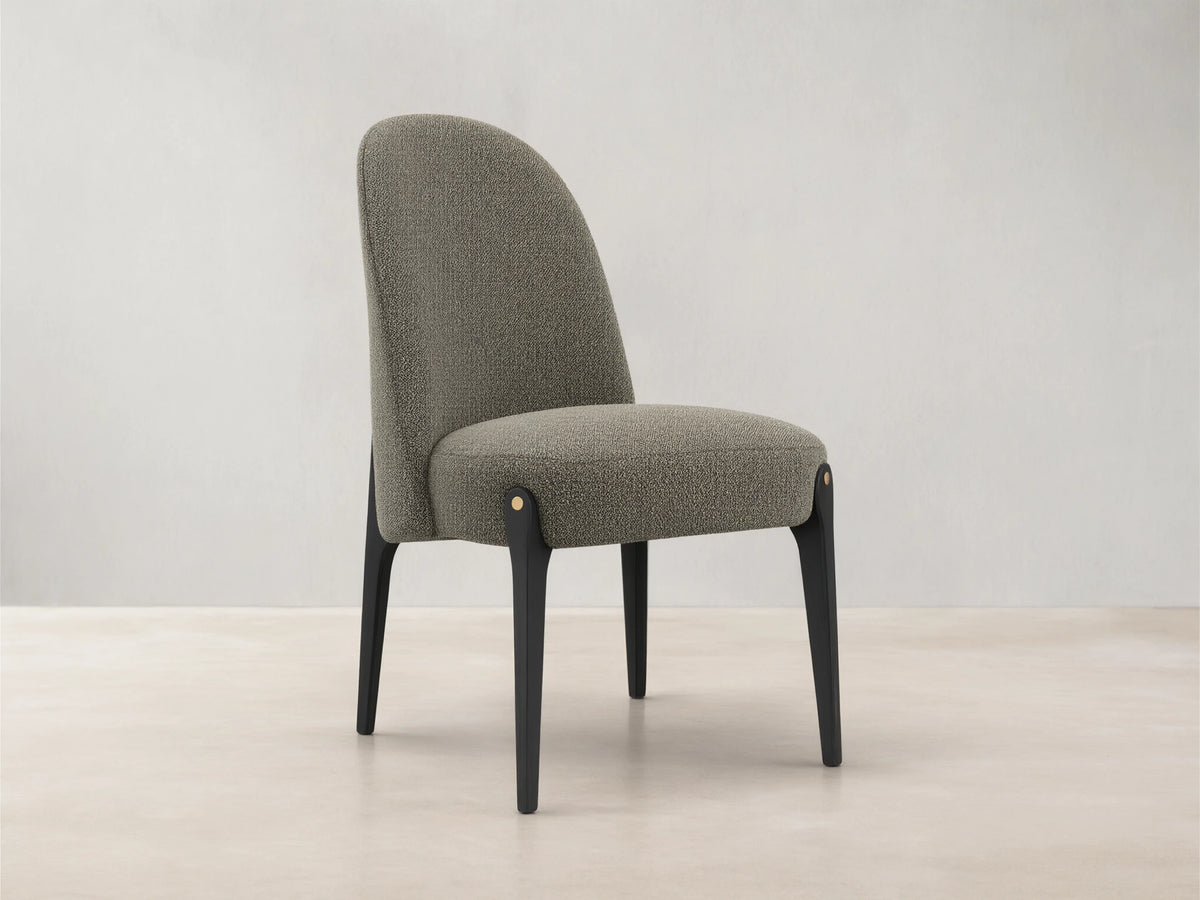 Bottoni Dining Chair, upholstered in light brown textured fabric, with dark legs and brass accents, angled on a wood floor.