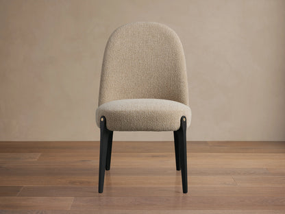 Bottoni Dining Chair with light beige textured upholstery, dark legs, and brass accents, angled slightly right on a wood floor.