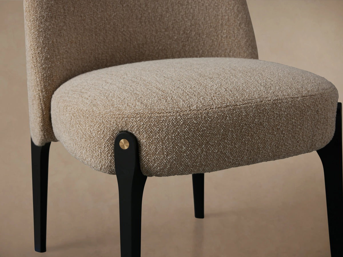 Bottoni Dining Chair, light beige textured upholstery, rounded back, dark black legs with brass tacks, front view.