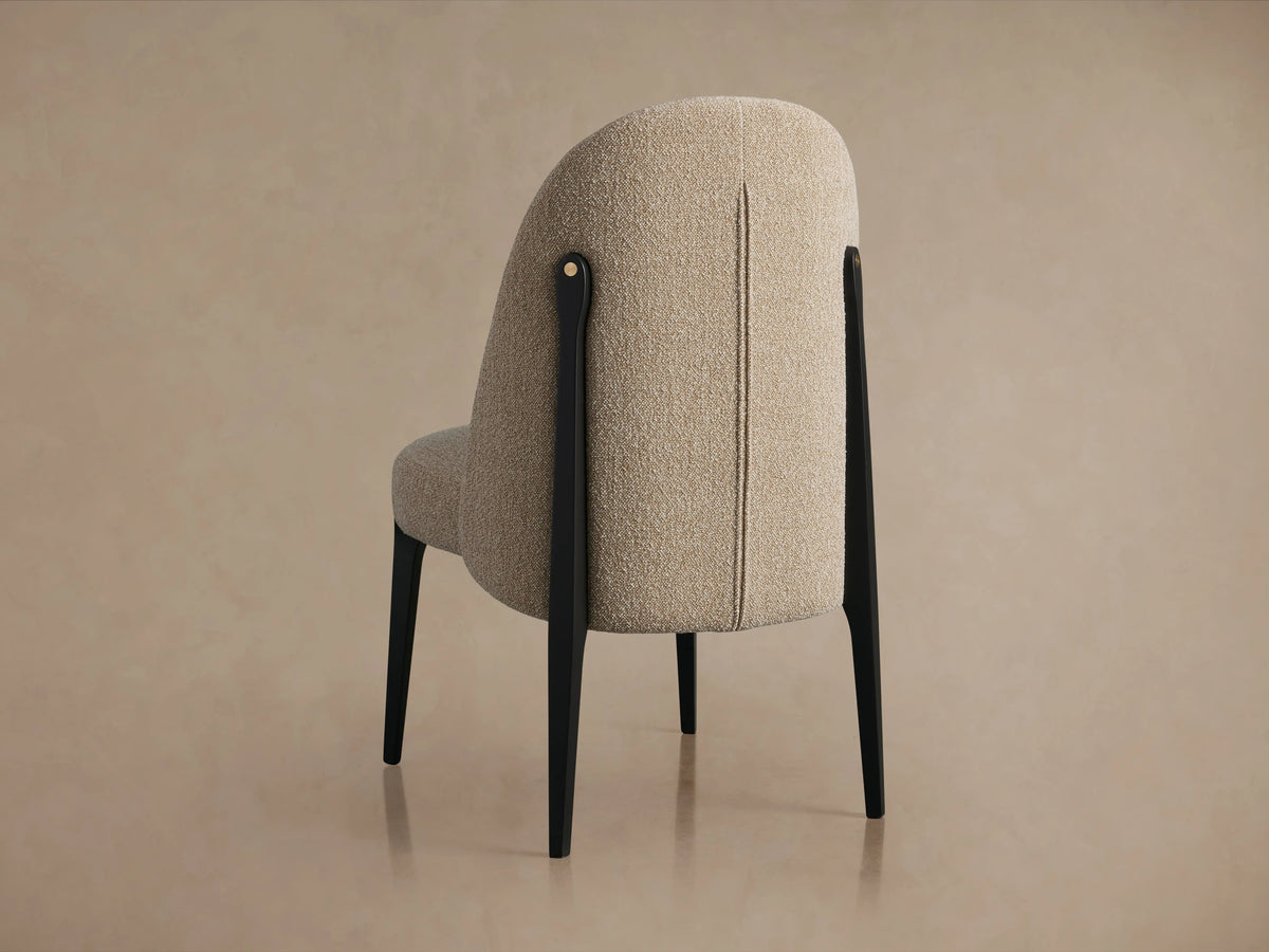 Bottoni Dining Chair with light beige textured fabric upholstery, sleek black legs, and brass accent, angled front-right.