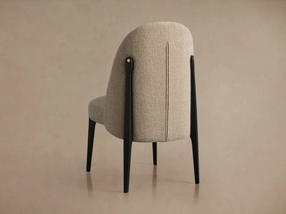 Bottoni Dining Chair with light beige textured fabric upholstery, sleek black legs, and brass accent, angled front-right.