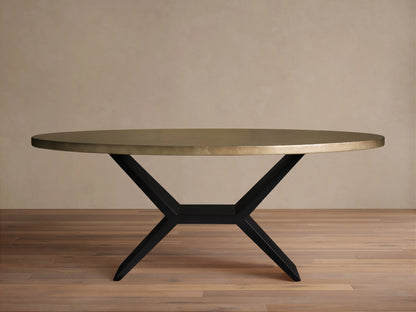 Oval dining table with a brass-toned recycled metal top and a striking black iron Vertex Base, against a neutral wall.