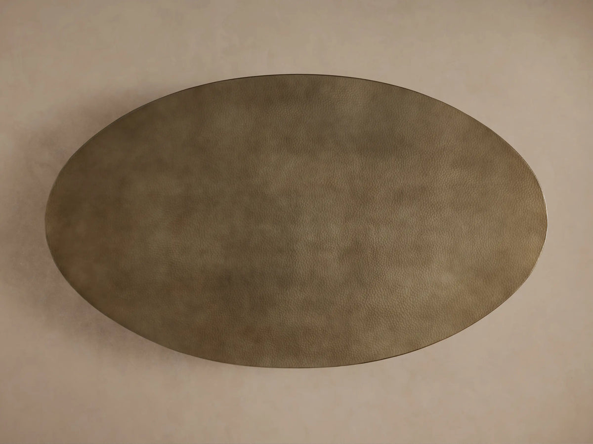Close-up of Recycled Metal Dining Table. Oval brass-toned, hand-hammered tabletop with butterfly stamp, black Vertex base.
