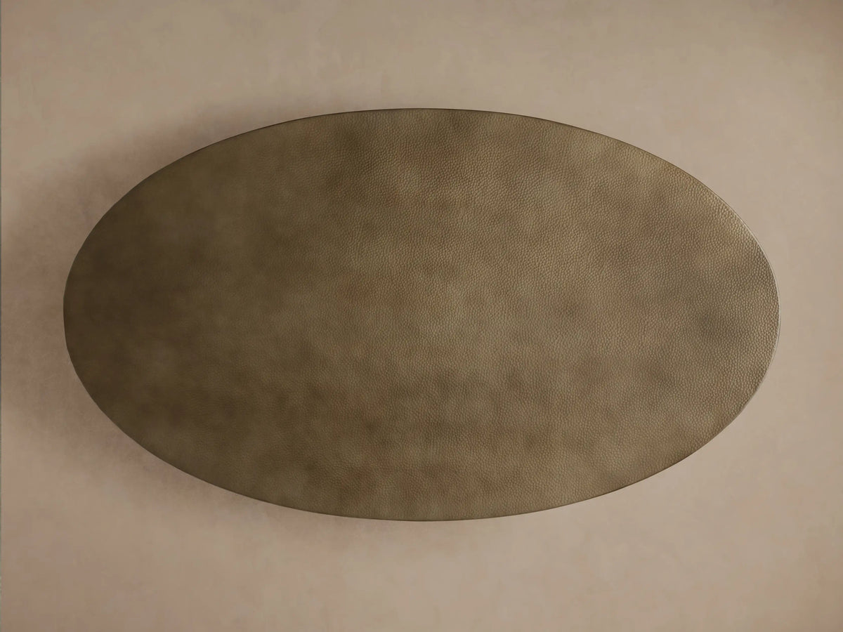 Angled close-up of Recycled Metal Dining Table. Oval hammered bronze tabletop with monarch butterfly stamp sits on a black Vertex Base.