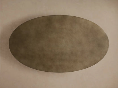 Angled close-up of Recycled Metal Dining Table. Oval hammered bronze tabletop with monarch butterfly stamp sits on a black Vertex Base.
