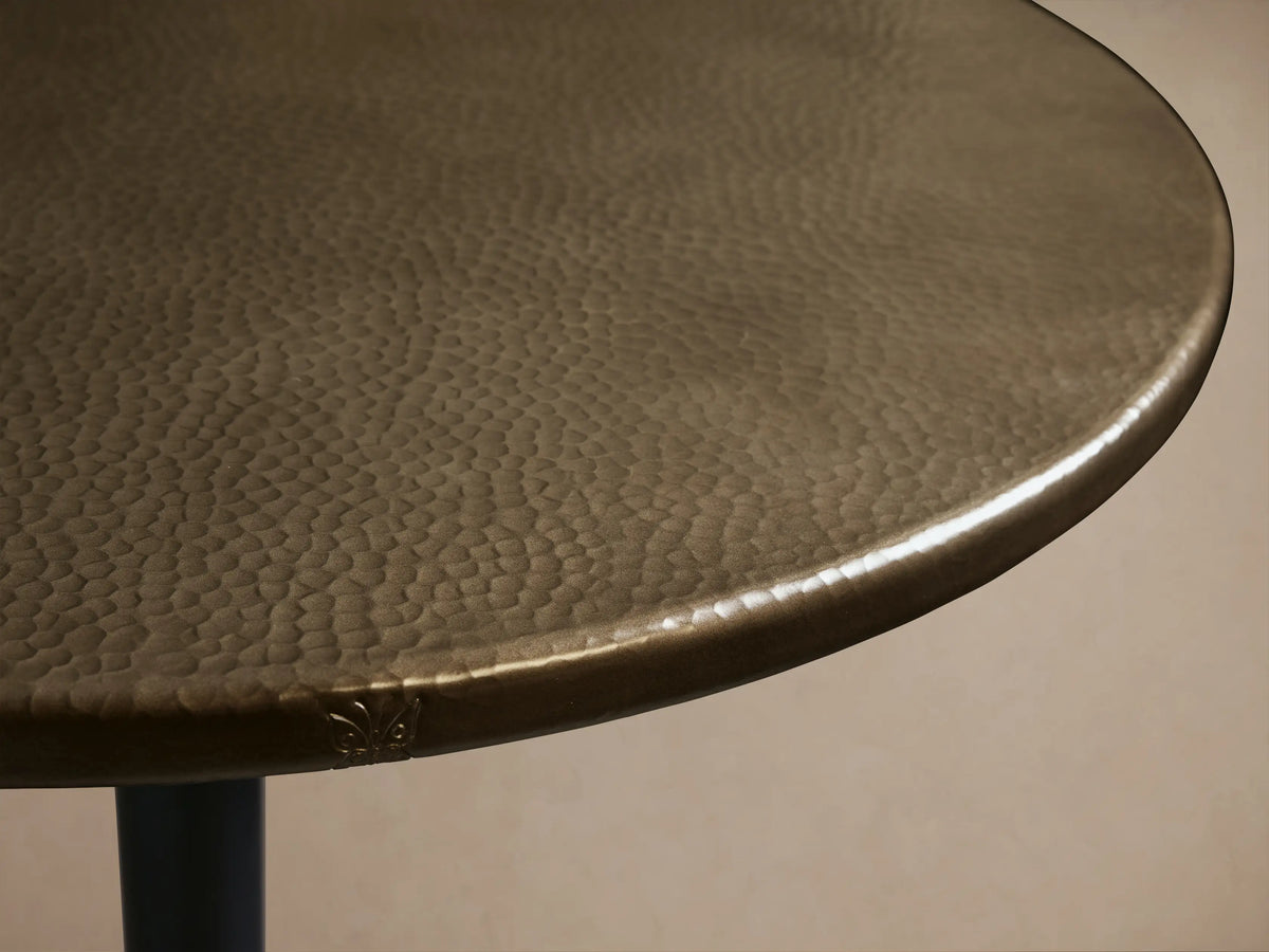 Recycled Metal Bistro Table featuring a round, brass-finished metal top and a black Wade base on a wooden floor.