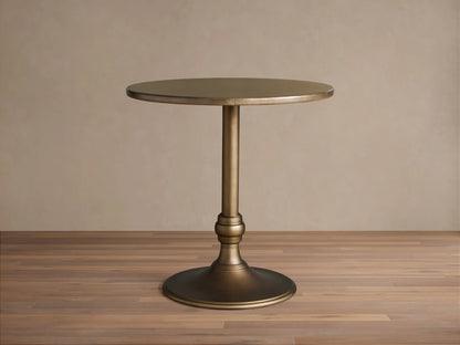 Round brass-finished recycled metal counter table with a single pedestal Wade iron base, centered on a wood floor.