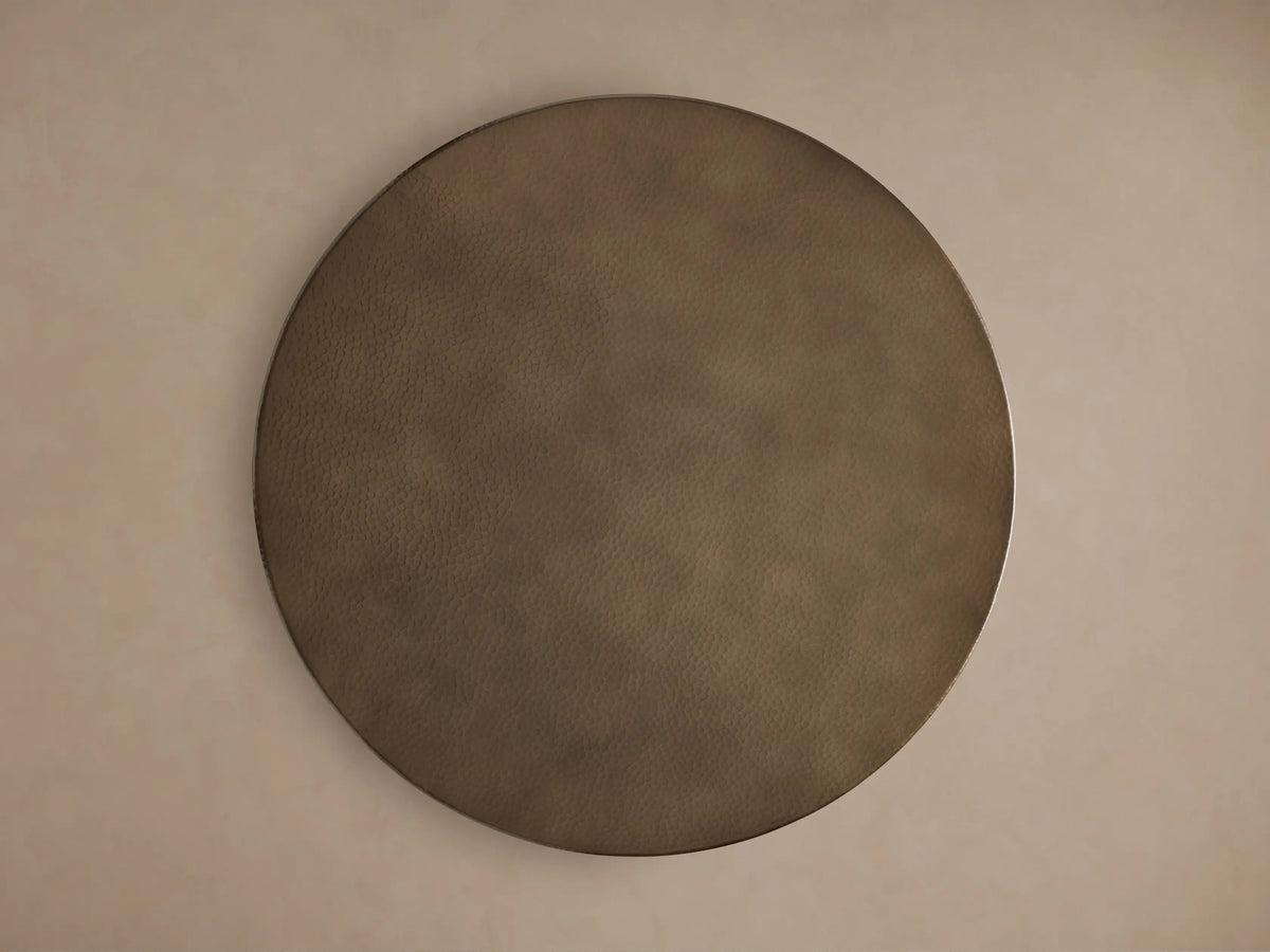 Close-up of a round, hammered brass-finished recycled metal counter table with an ornate embossed detail on the edge.