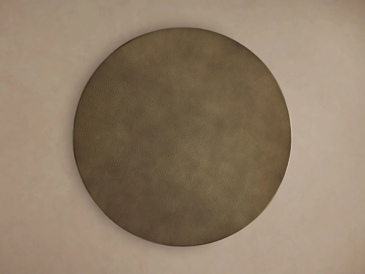 Round brass-finished hammered recycled metal bar table top close-up. Features an embossed mark, textured surface, & dark base.