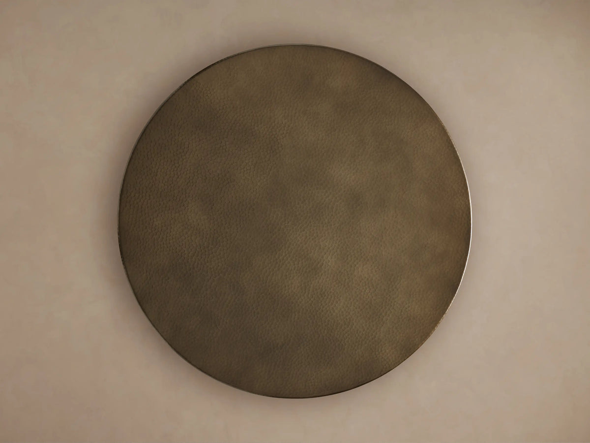 Close-up of a Recycled Metal Counter Table. Round, hammered brass-toned tabletop with a subtle sheen, black base.