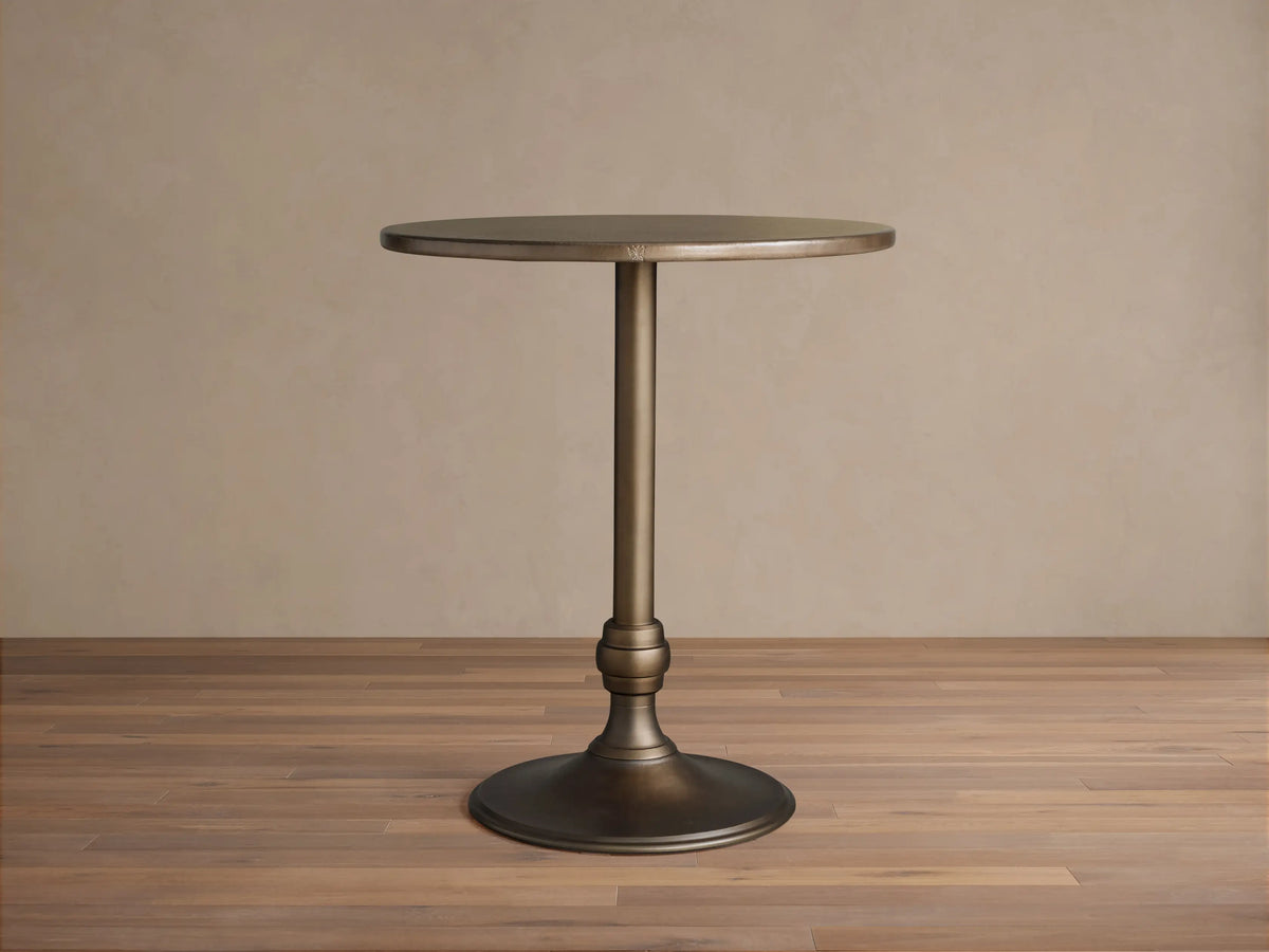 Recycled Metal Bar Table with a round bronze-colored top and a matching Wade base, standing on a wooden floor.